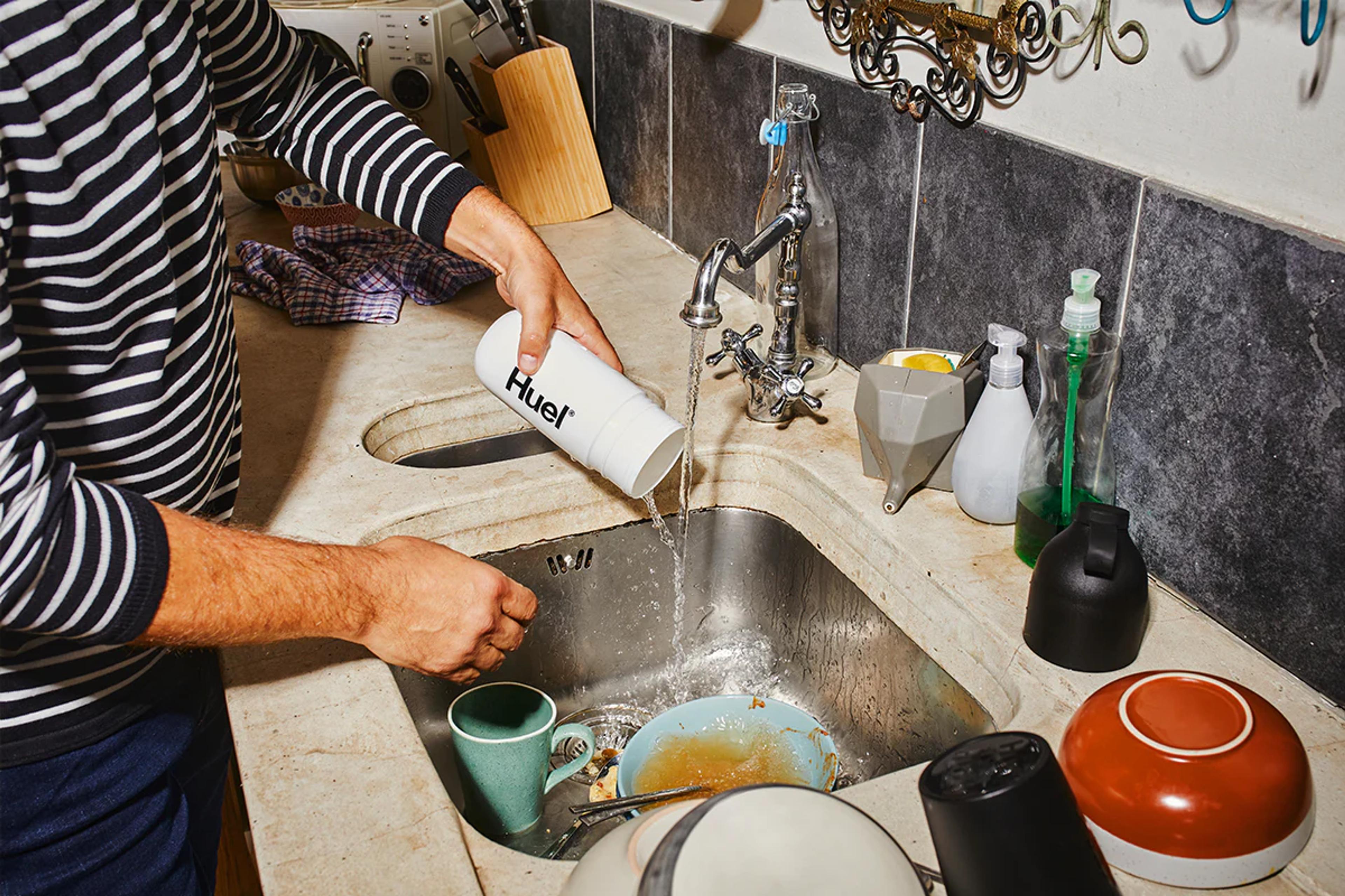 man cleaning their huel shaker in the sink which has dirty dishes in