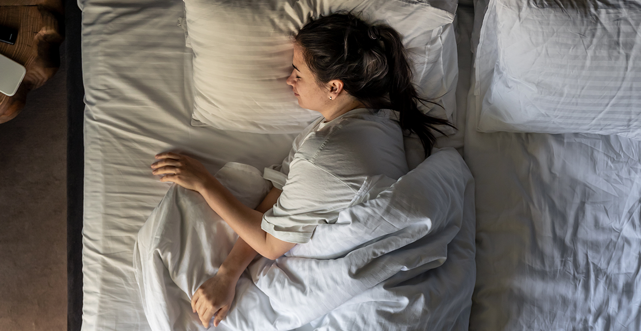 A woman on her side sleeping in a bed with white sheets and pillowcase