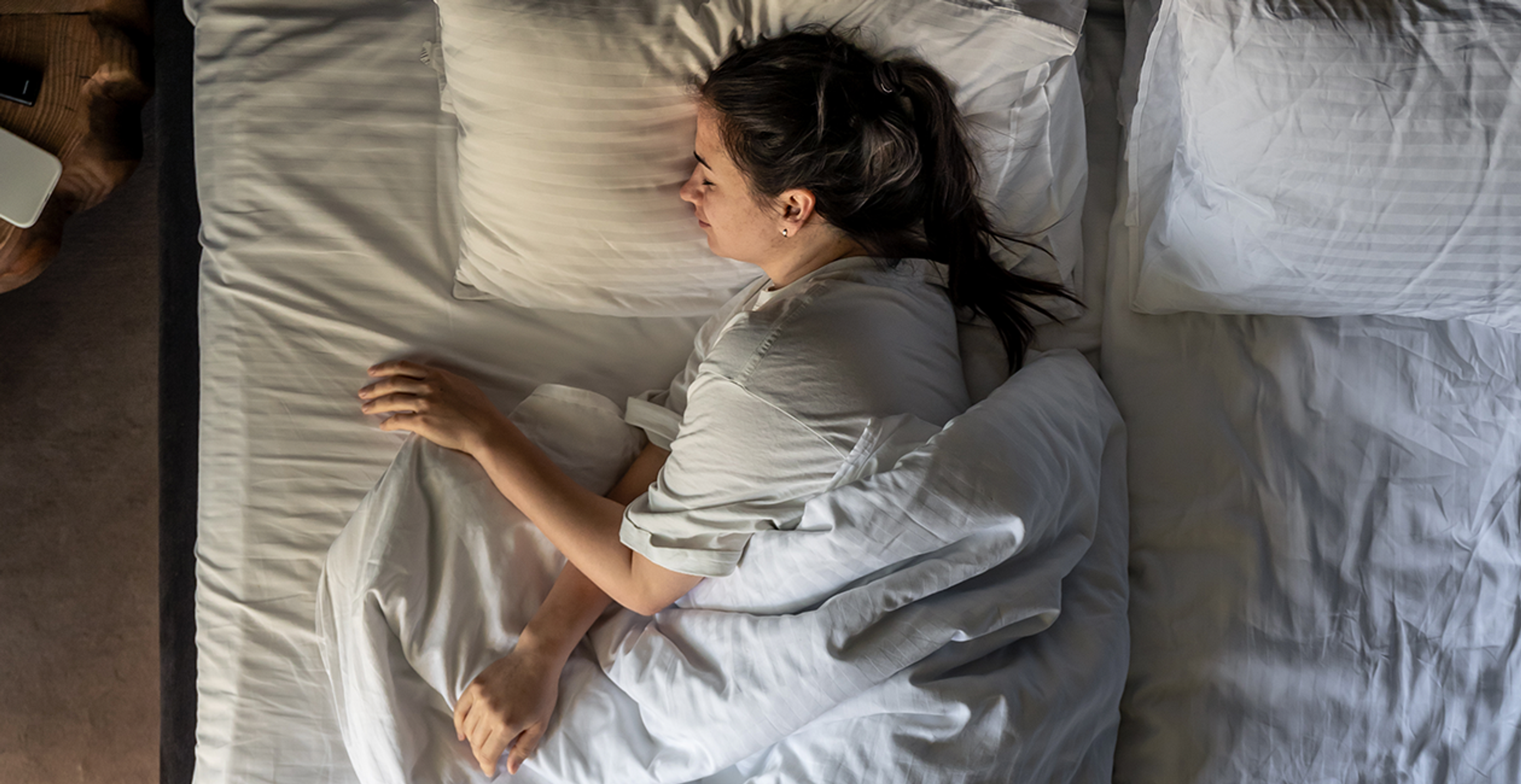 A woman on her side sleeping in a bed with white sheets and pillowcase