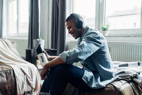 Man sat on sofa with headphones on holding a Huel shaker