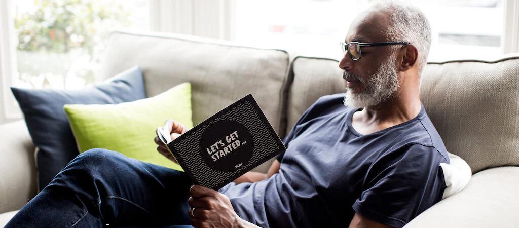 Man reading a Huel booklet on a grey sofa with a green cushion