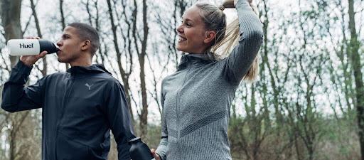 two people walking outside the man is drinking from a huel shaker and the woman is smiling