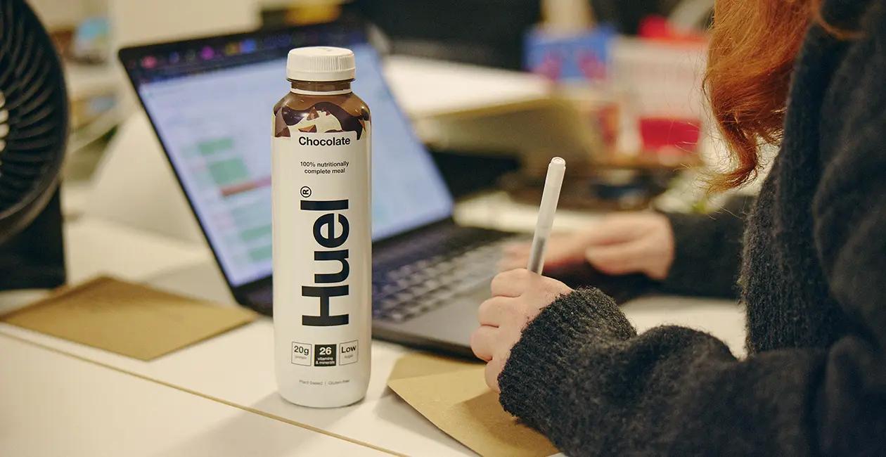 woman working at her desk on a laptop with a Huel Ready-to-drink next to her