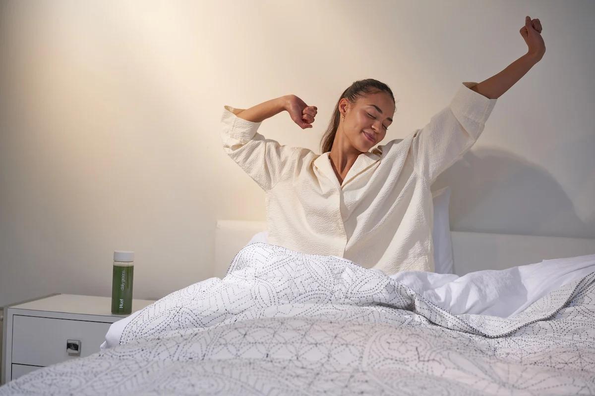 Woman waking up in bed with Huel Daily Greens mixed in a Huel bottle on the bedside table