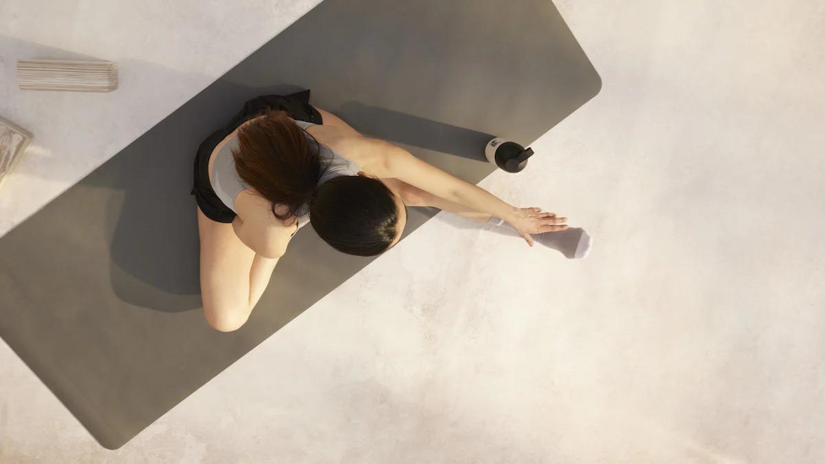 top down view of woman sat on a yoga mat stretching with a huel shaker next to her