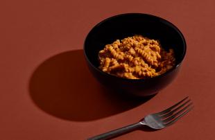 Close-up of H&S Bolognese Bowl set against a red background next to a metal fork