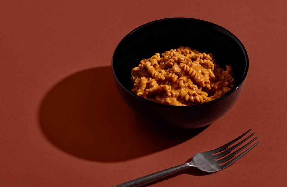 Close-up of H&S Bolognese Bowl set against a red background next to a metal fork