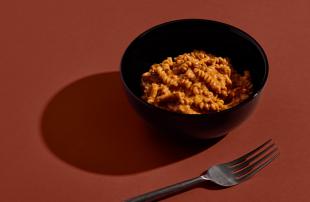 Close-up of H&S Bolognese Bowl set against a red background next to a metal fork