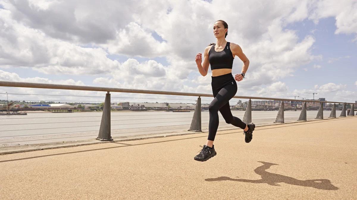 woman running on path alongside a river breathing heavily