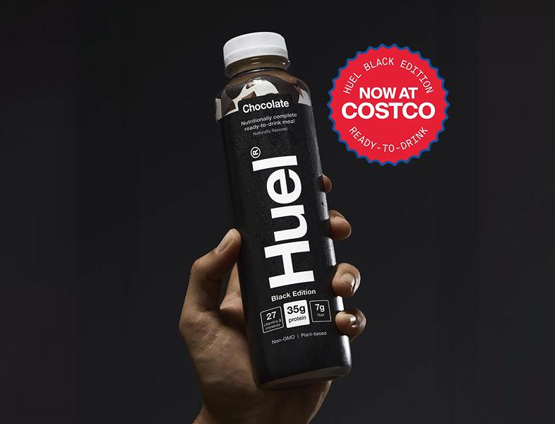 Two Huel Black Edition ready-to-drink meal bottles in Chocolate and Strawberry Banana flavors with a green badge stating “Now at Costco.” The bottles are sleek with bold white text on black labels.
