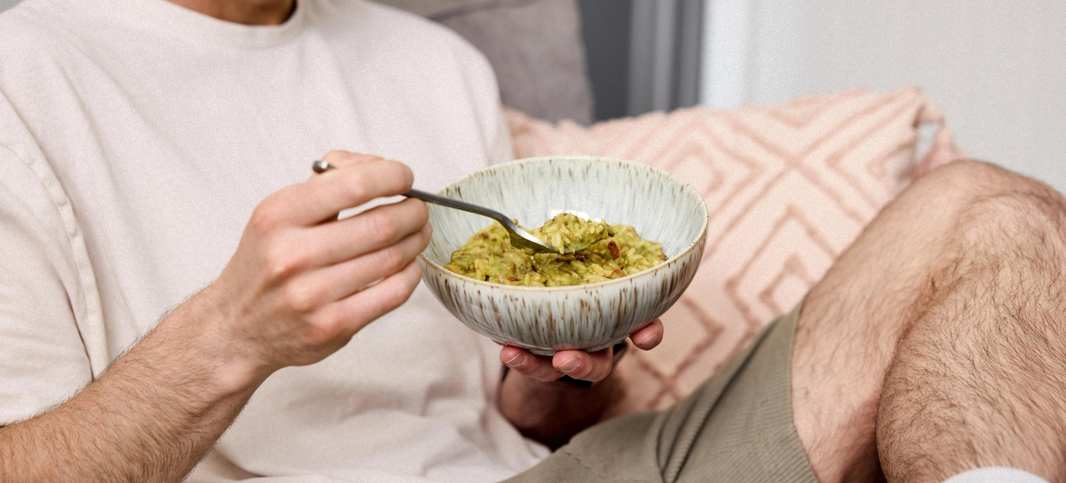 Image of a man smiling while eating from a pot of Huel Hot & Savoury vegan instant meal