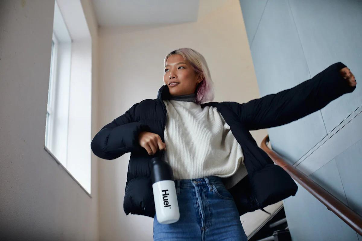 woman walking down the stairs whilst holding a huel shaker