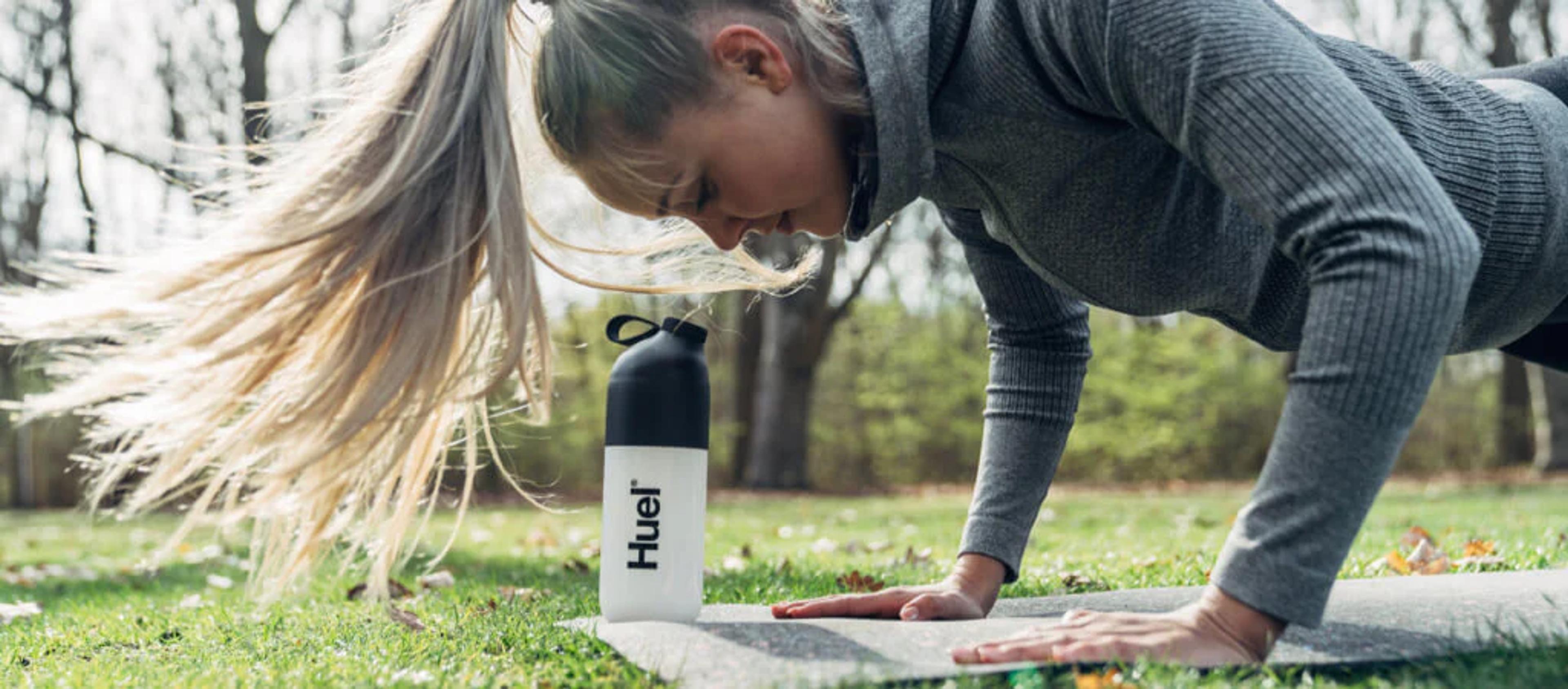 Woman doing press-ups outside with Huel shaker next to her