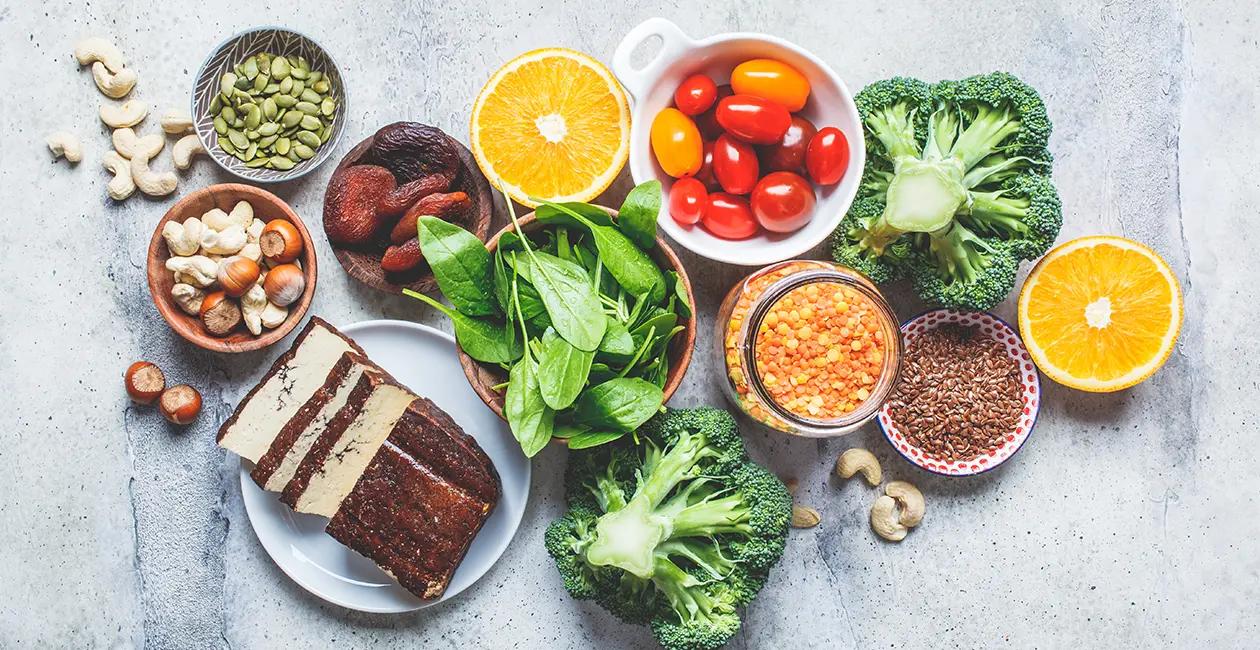 a variety of healthy foods in different bowls including broccili cherry tomatos spinach oranges and more