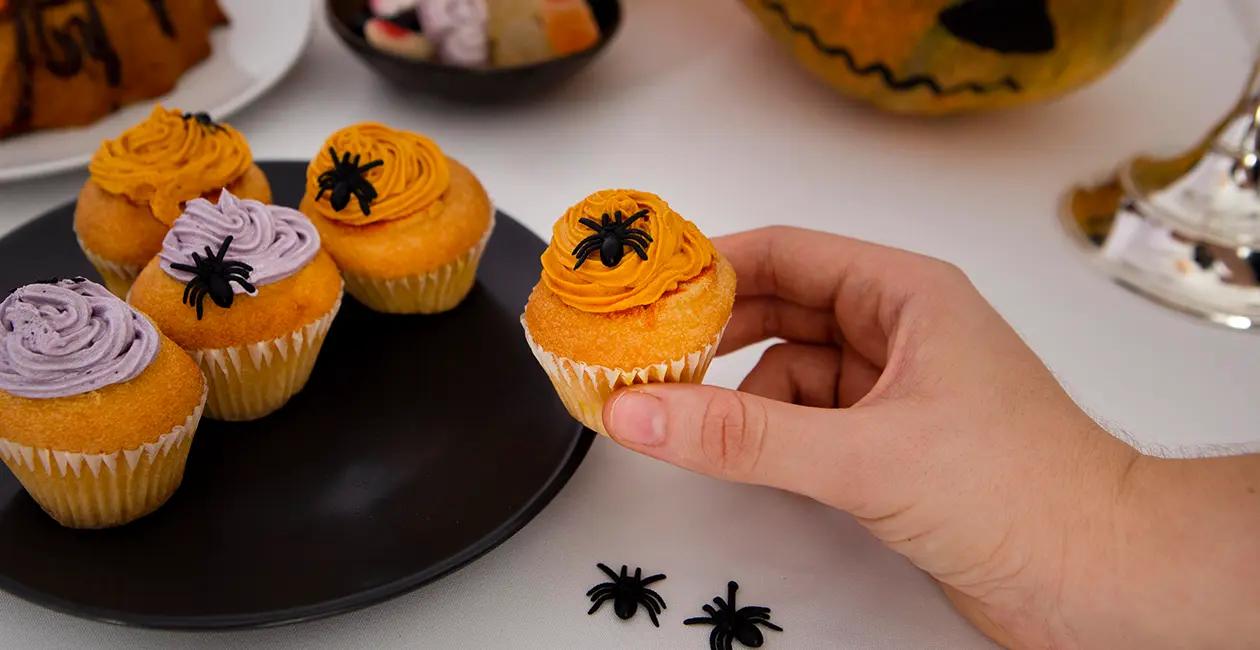 someone taking a halloween cupcake from a plate of cupcakes with icing spiders on top