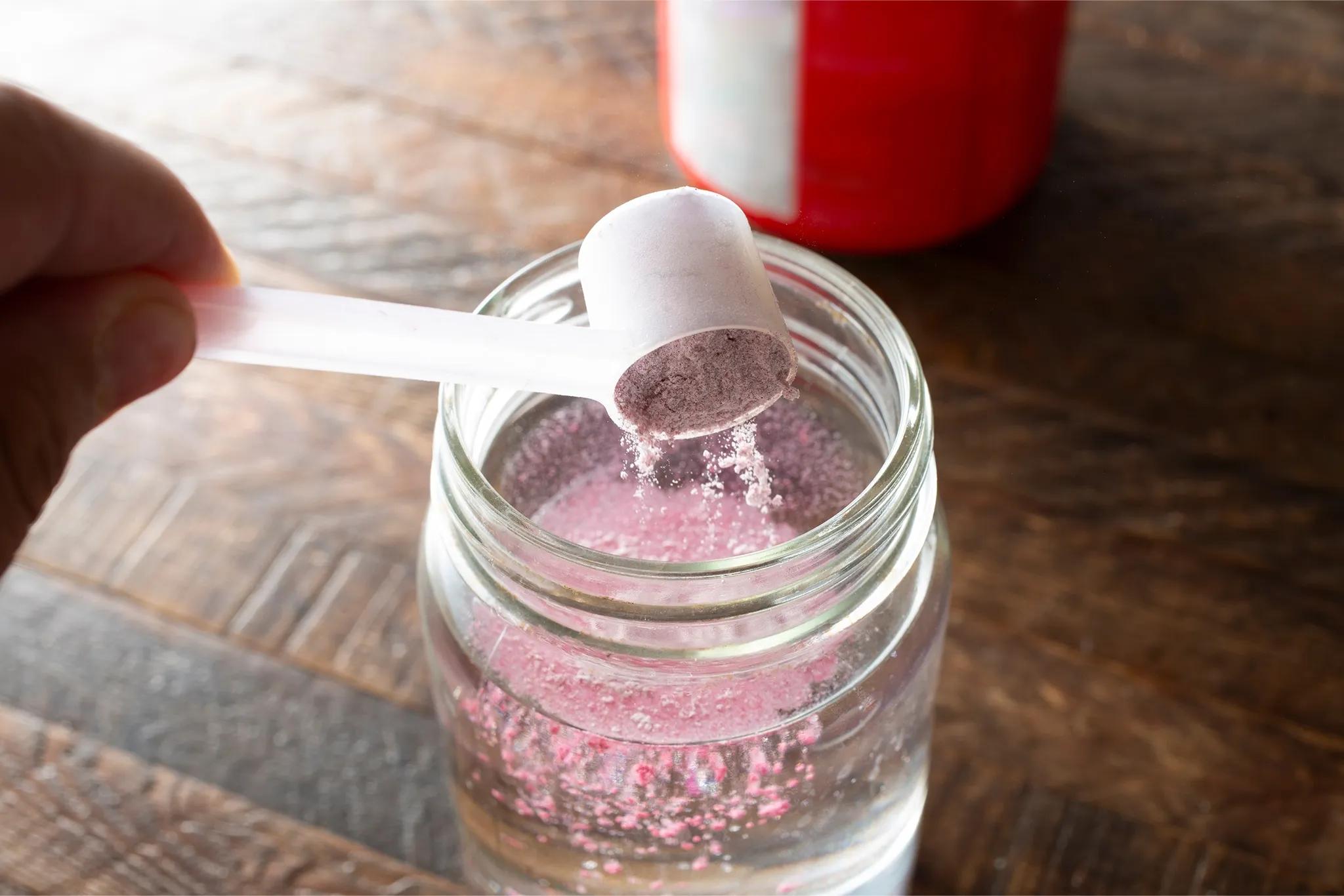 someone pouring powdered electrolytes into a shaker with water in it