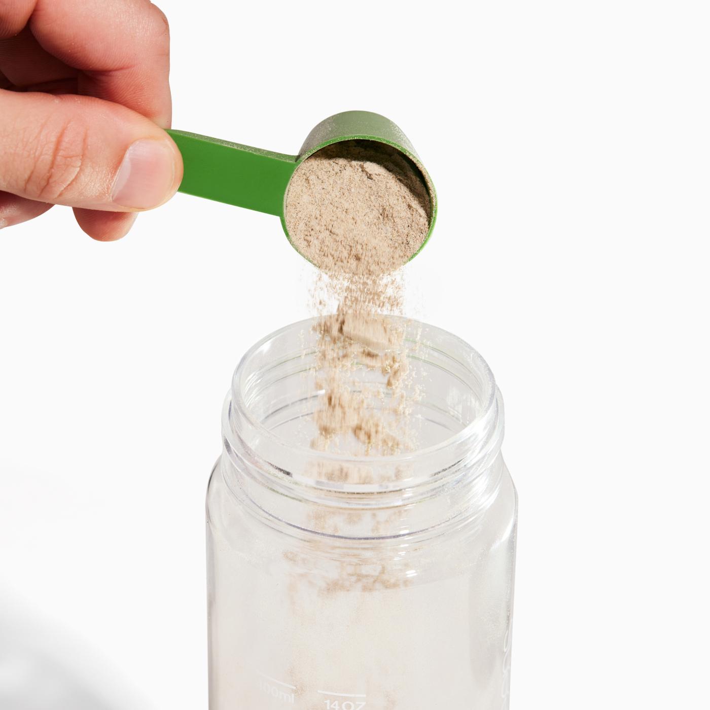 Pouring a scoop into Greens clear bottle