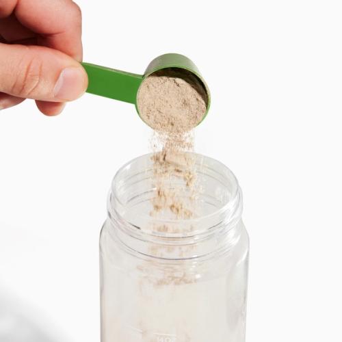 Pouring a scoop into Greens clear bottle