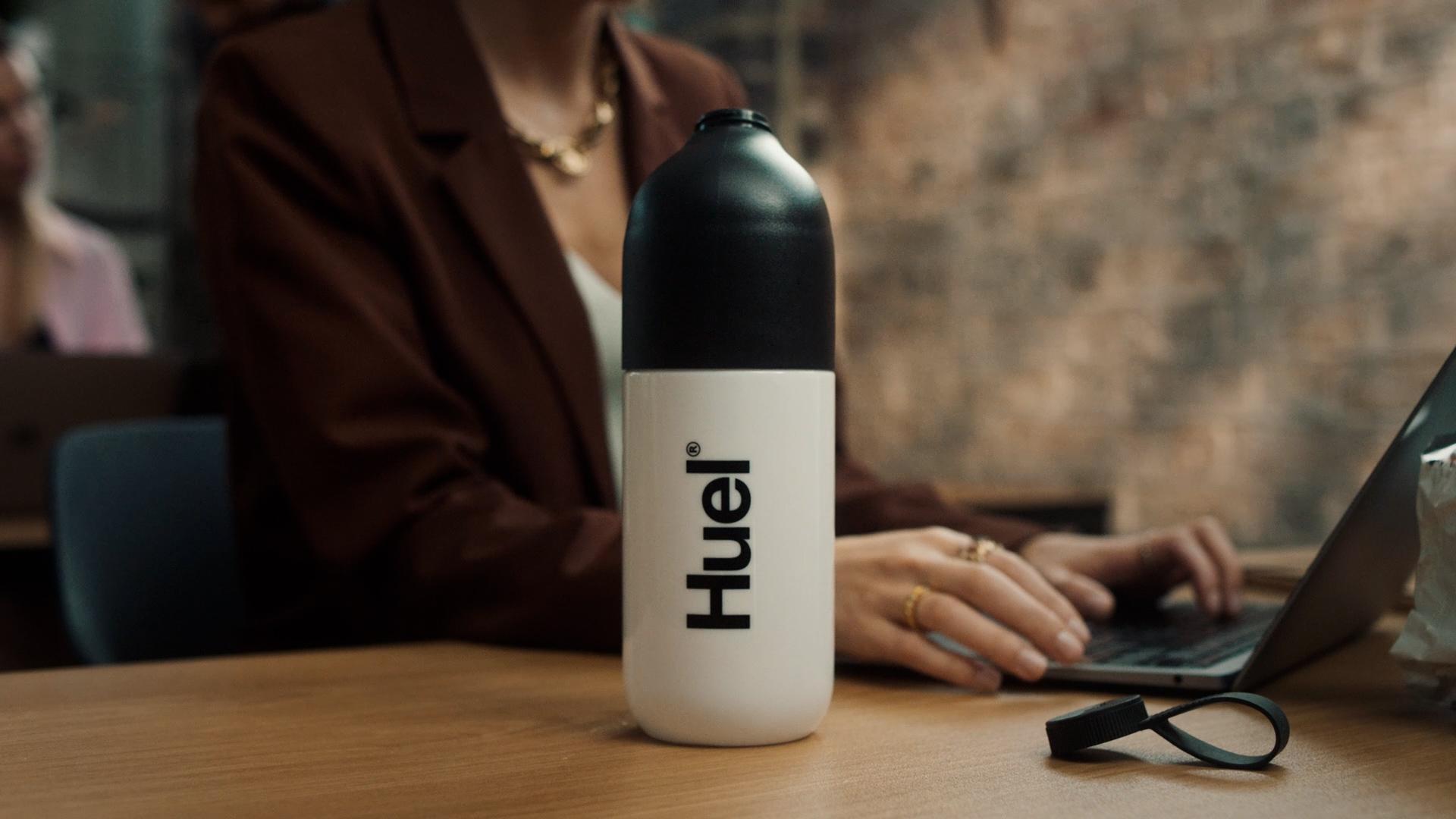woman working on a laptop with a huel shaker in the foreground