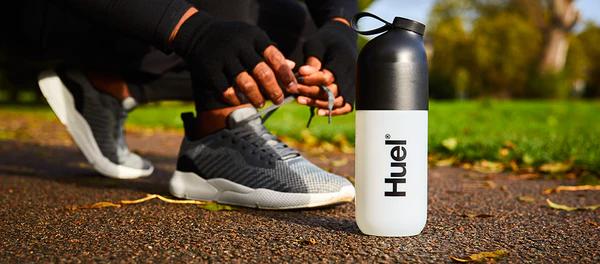 person bent over tying their shoelace on a path outside with a huel shaker stood on the ground next to them