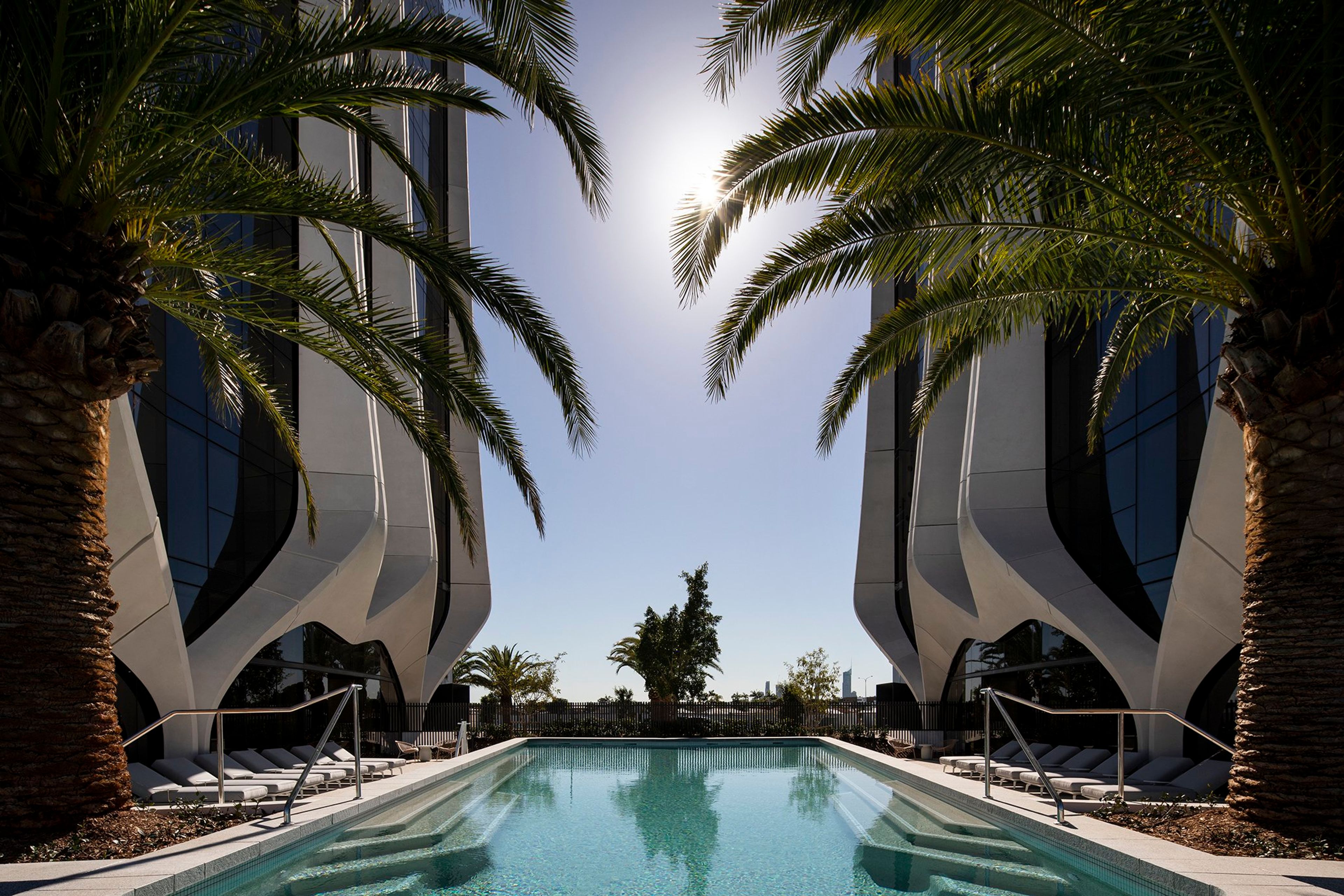 a large swimming pool surrounded by palm trees in front of a building .