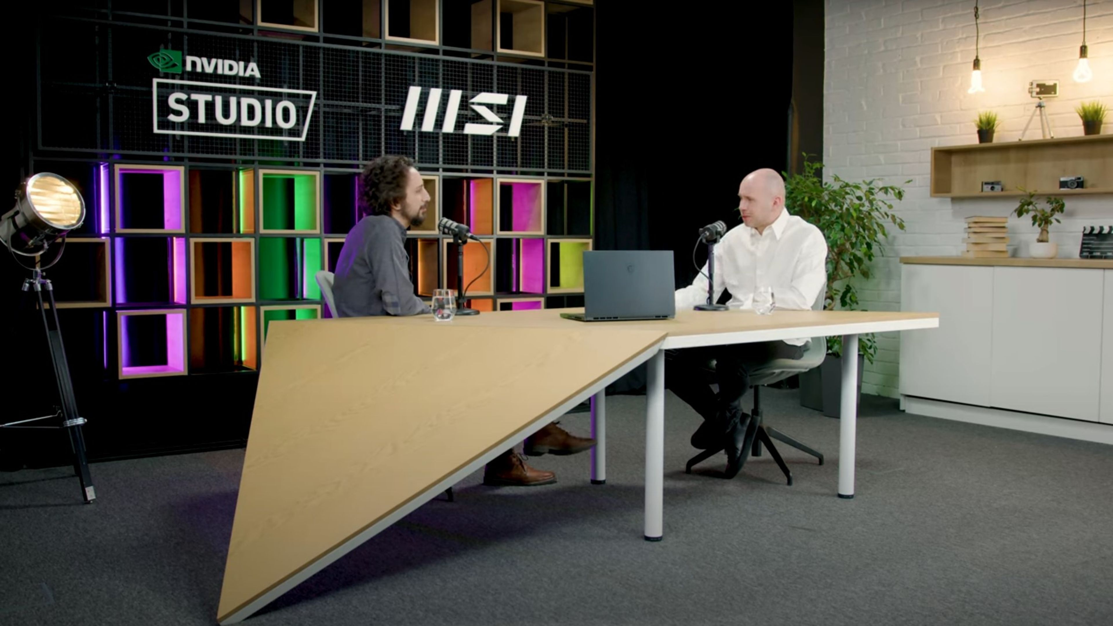 two men are sitting at a table with a laptop and talking into microphones .