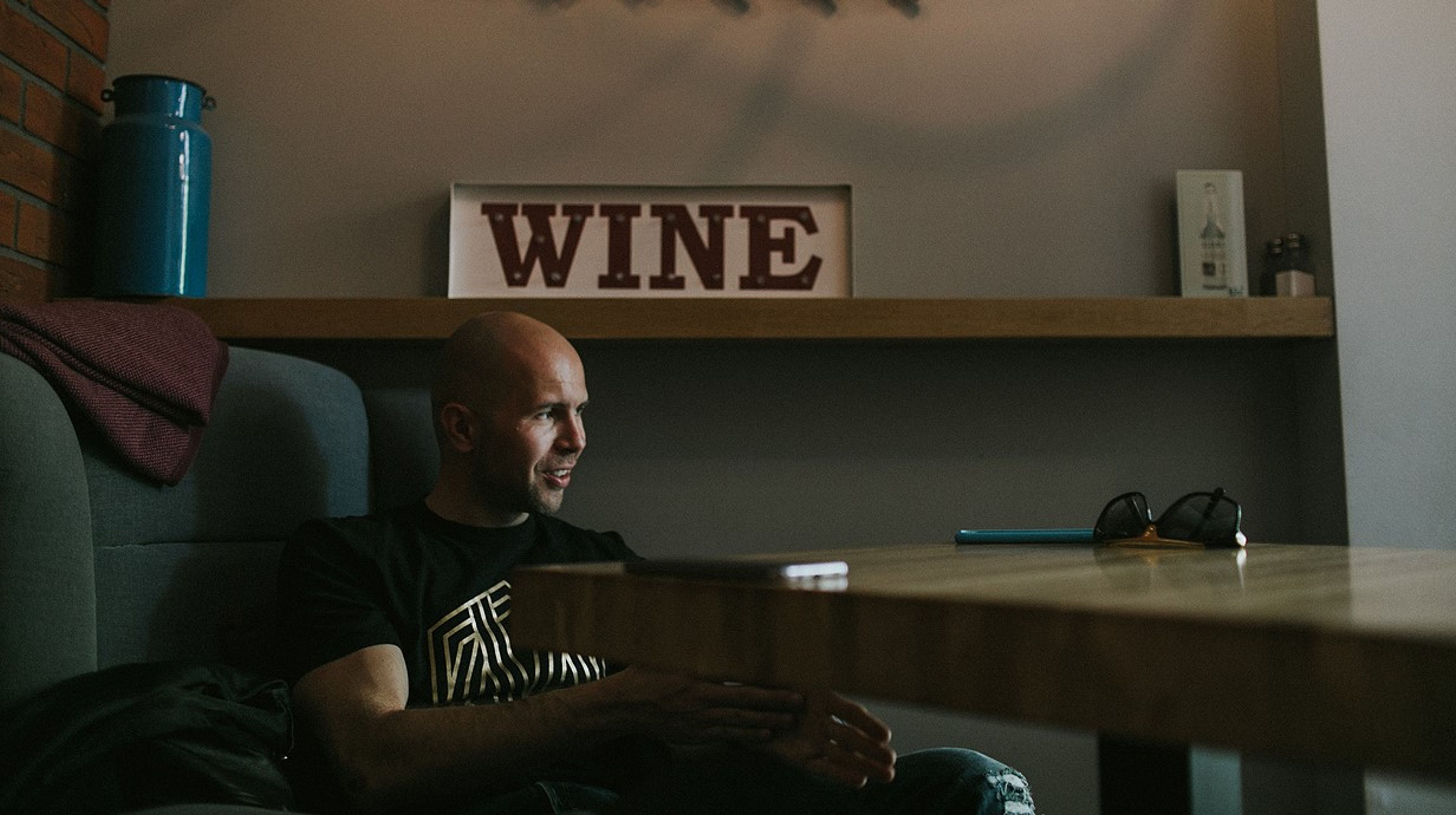 a man is sitting at a table in front of a sign that says wine .