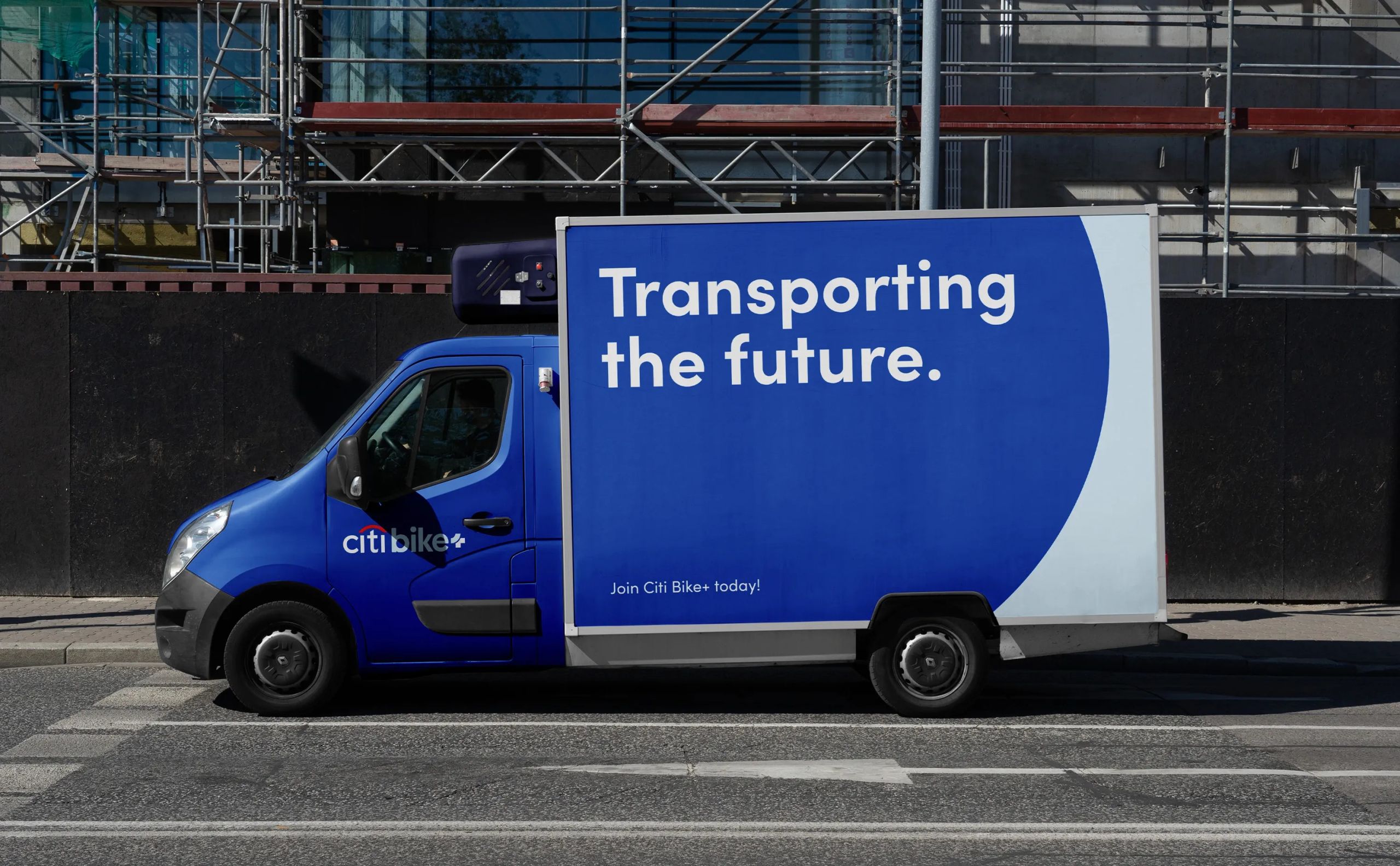 Mockup of a branded Citi Bike+ van parked on the street, featuring a bold blue graphic with the phrase “Transporting the future.” promoting sustainable urban mobility.