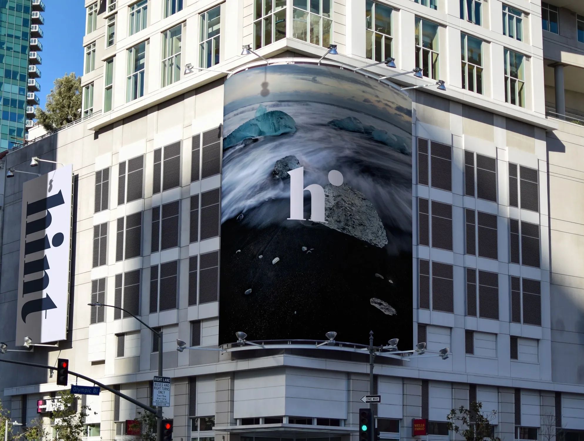 Mockup of a large-scale Hint brand installation wrapping a city building, featuring the “h” logo over an icy shoreline photo, promoting a clean, nature-inspired identity in an urban setting.