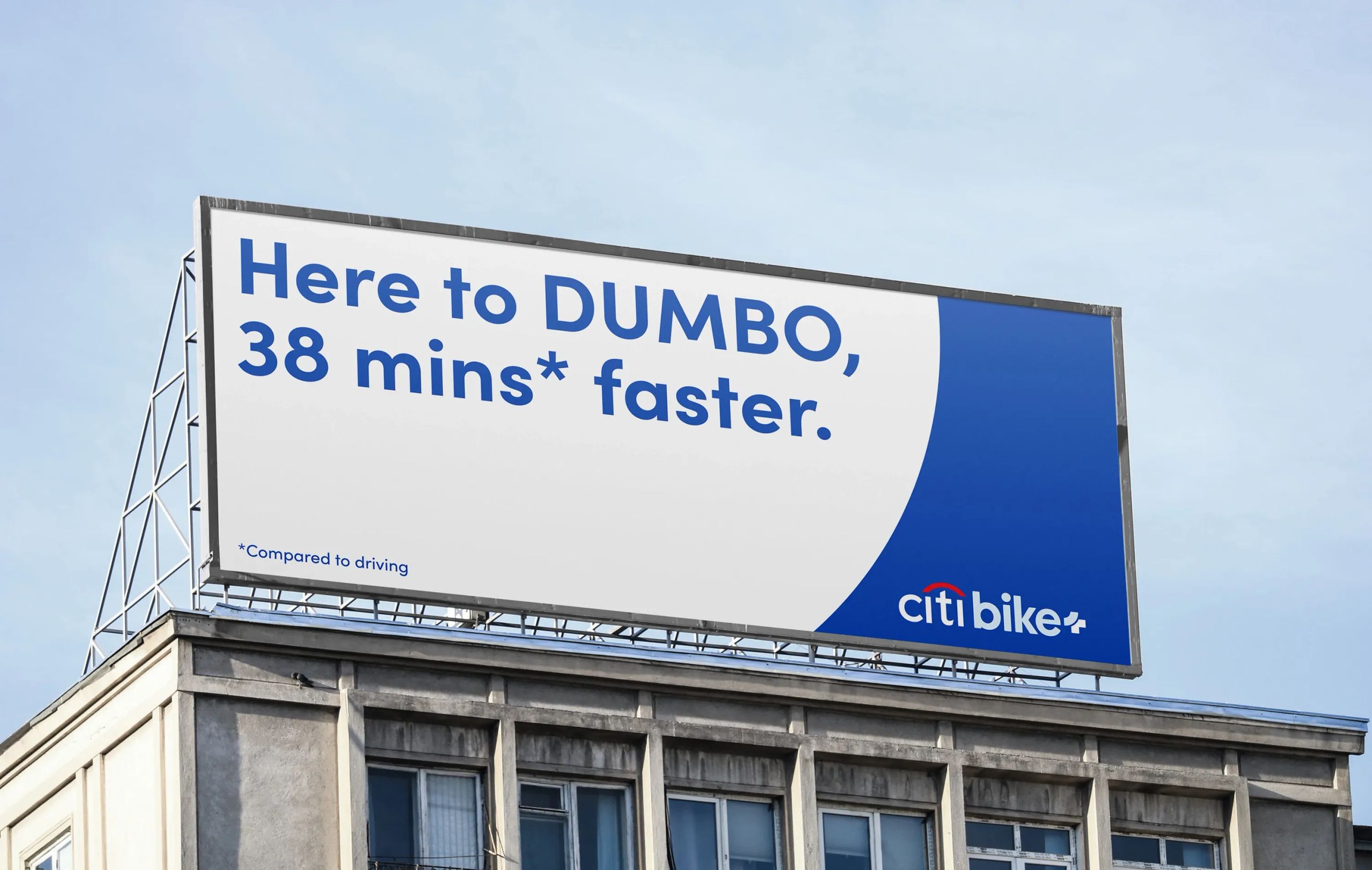 Billboard mockup for Citi Bike+ promoting faster commute times, reading “Here to DUMBO, 38 mins* faster,” with a note indicating the comparison is to driving. Set against a clear sky on top of a concrete building.