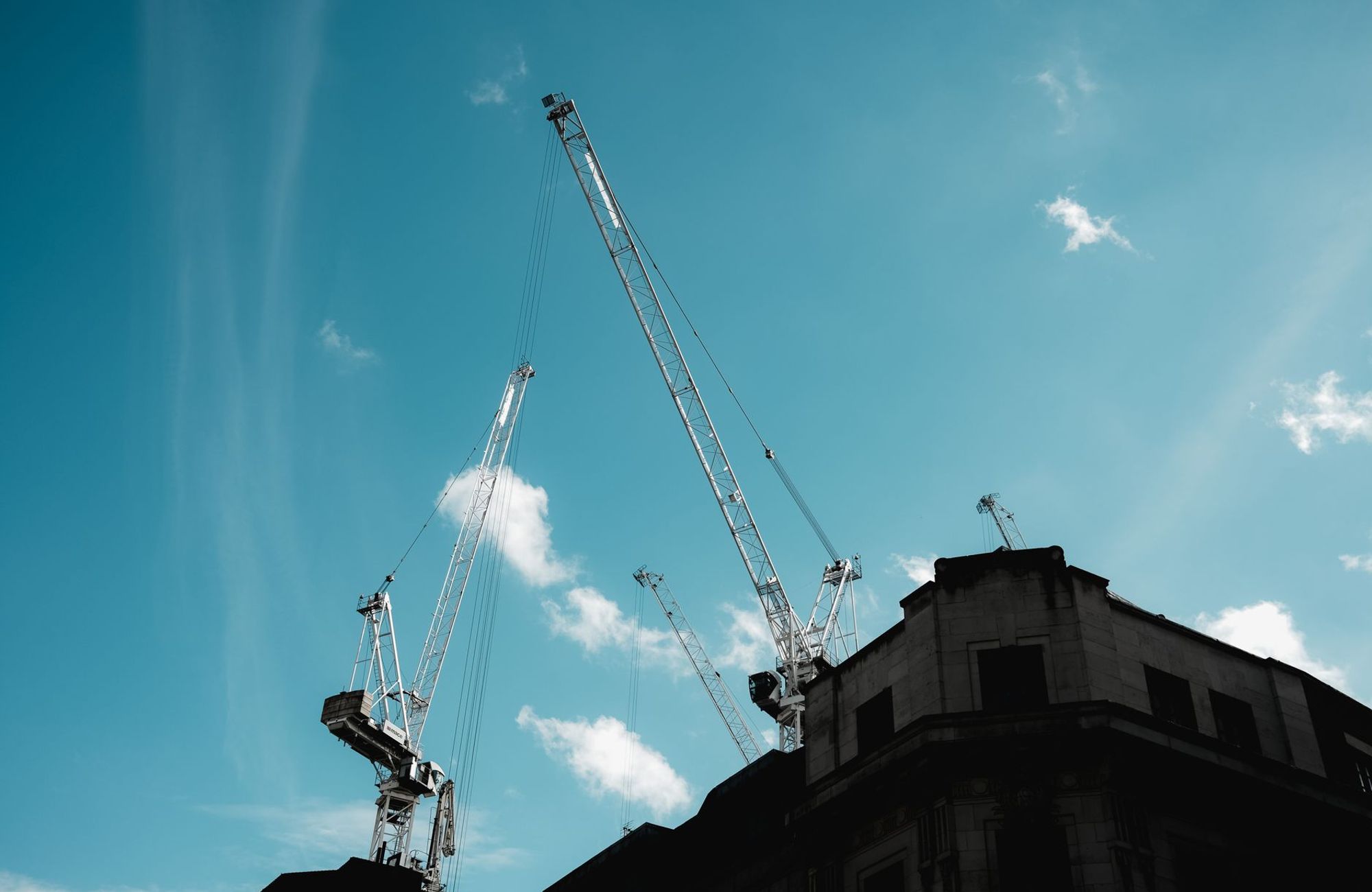 Silhouetted construction cranes extend into a clear blue sky. (Foto: Airam Dato-on / Pexels)
