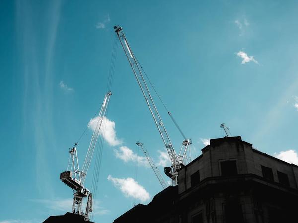 Silhouetted construction cranes extend into a clear blue sky. (Foto: Airam Dato-on / Pexels)