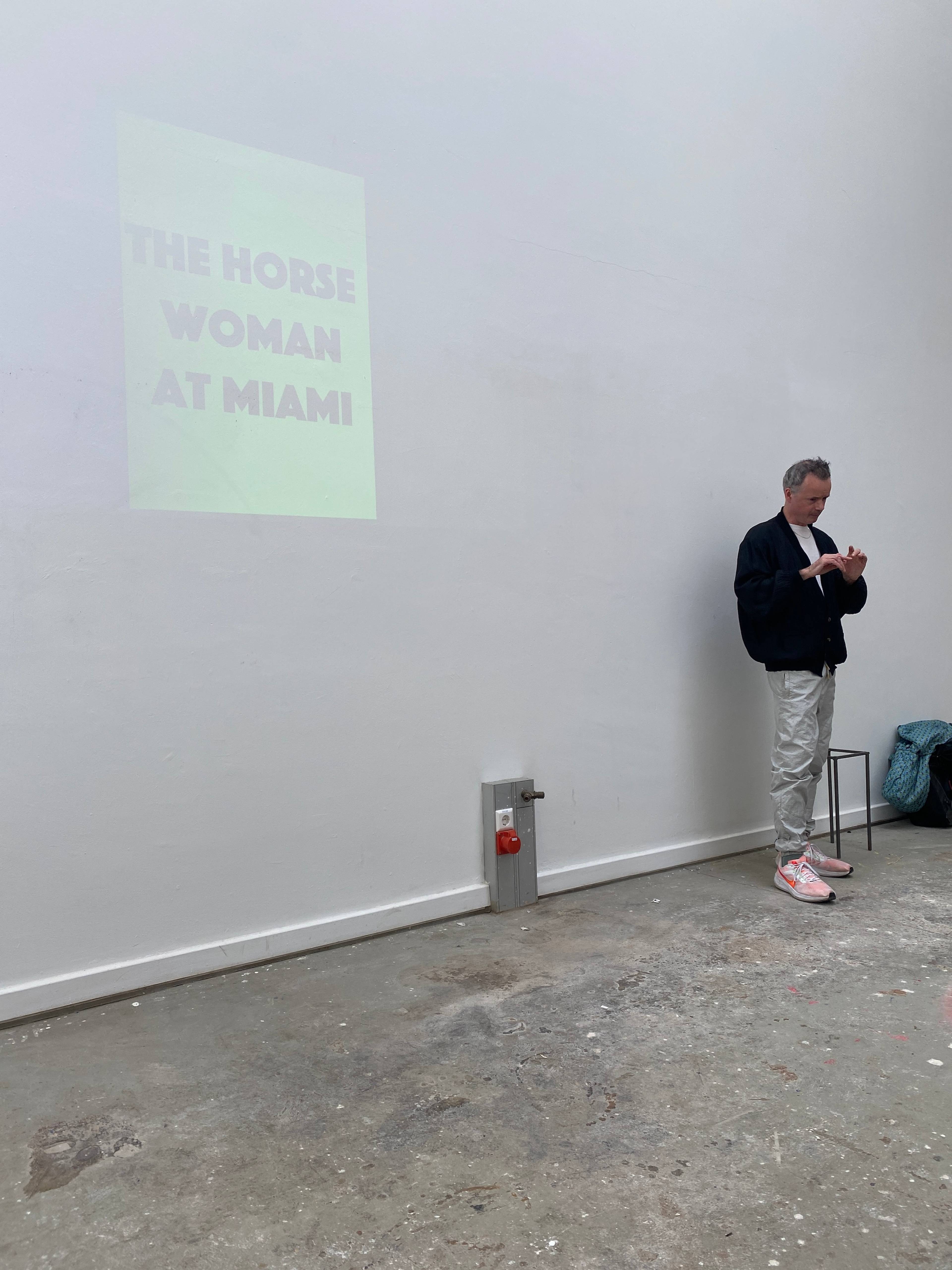 Andrew Cannon speaking during his lecture titled Welcome to the Jungle, with presentation visuals in the background, Kunstakademie Karlsruhe, 2024