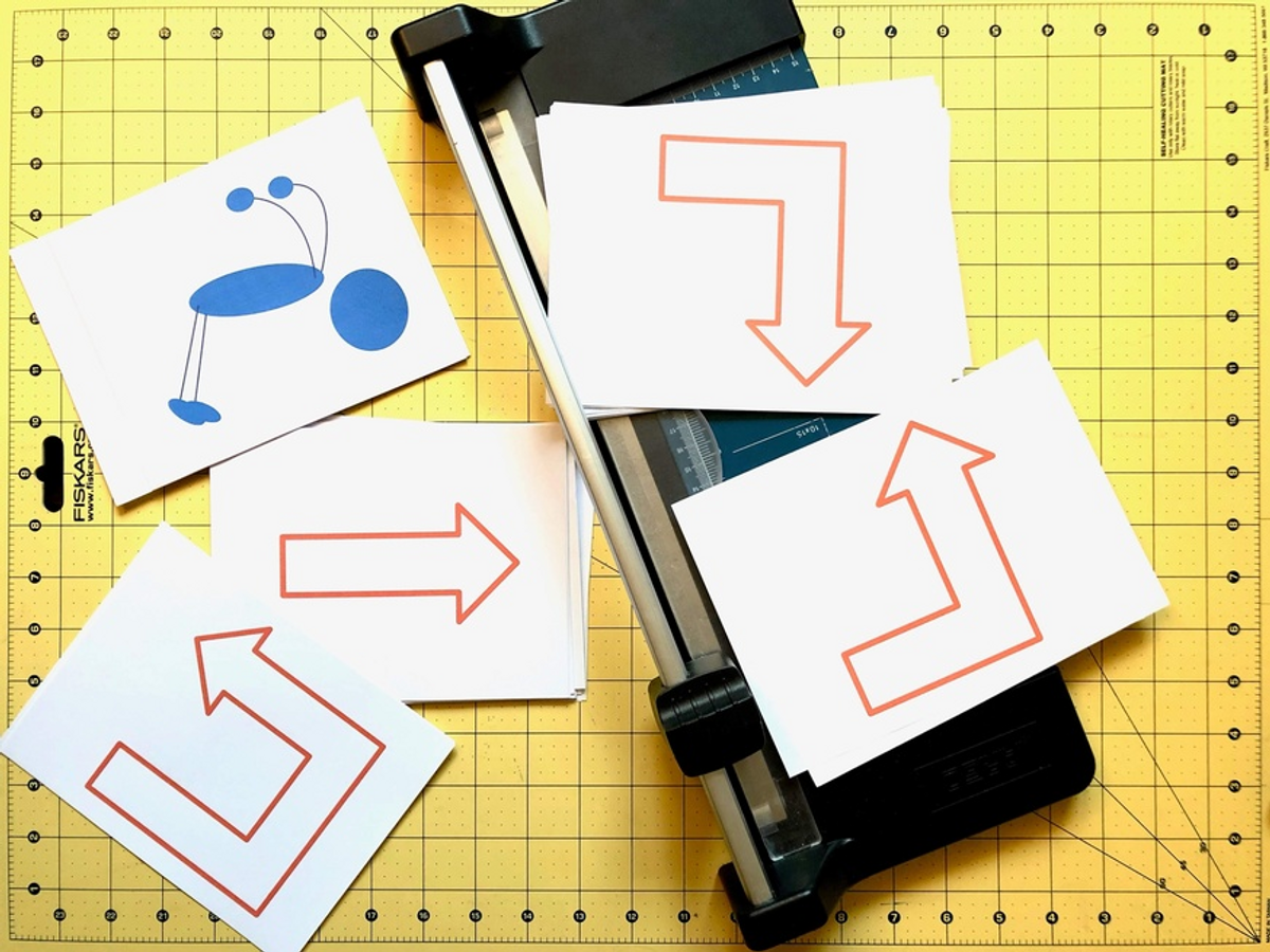 Ark med piler og figurer ligger på et gult bord med en papirkutter