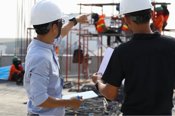 To personer med vernehjelm diskuterer arbeidet på en byggeplass.