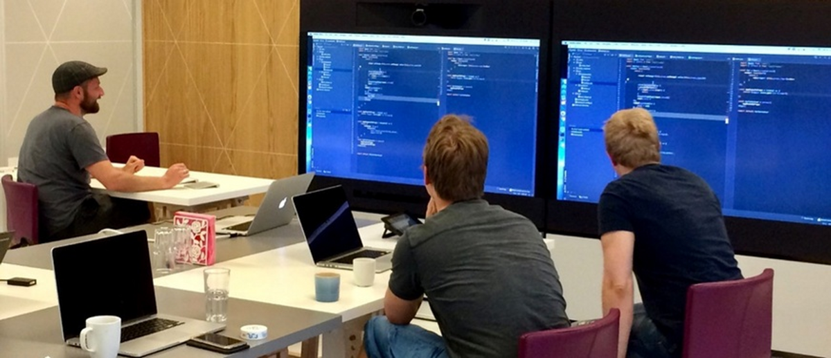 Tre menn som mob-programmerer foran to større skjermer.