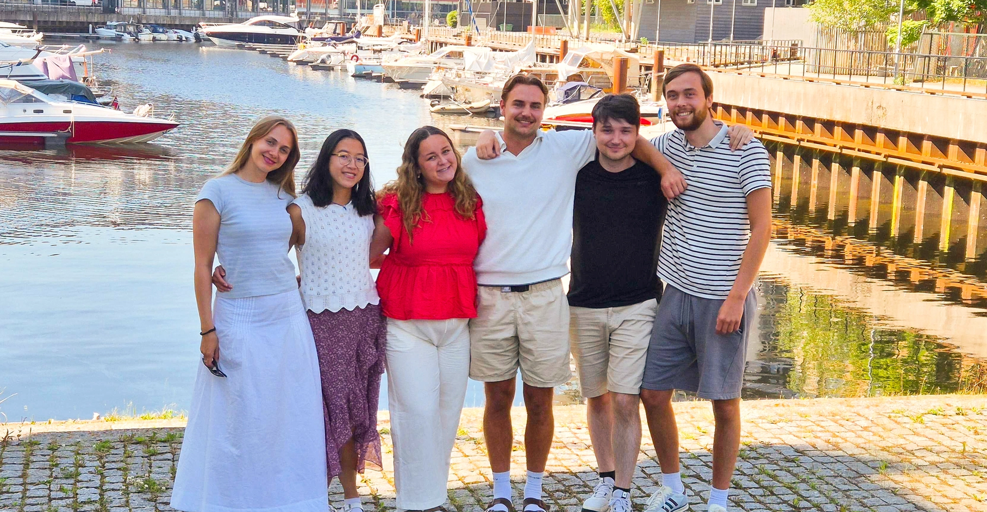 De seks sommerstudentene holder rundt hverandre og smiler.