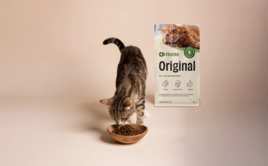 Katt som äter mat ur foderskål. FirstVet Original kattfoder påse i bakgrunden.
