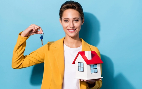 Smiling real estate agent holding up a house key and a small model house