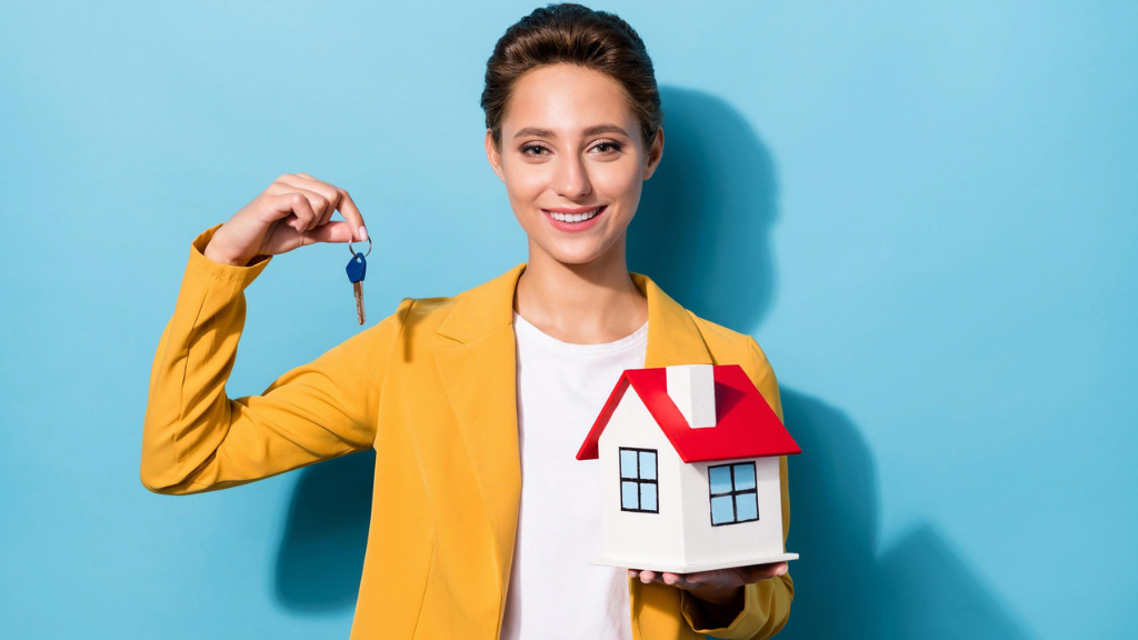 Smiling real estate agent holding up a house key and a small model house