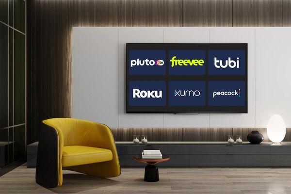 A living room with a yellow armchair. A large flat screen TV on the wall behind the armchair. The TV has the logos of several FAST channels including Tubi and Roku. 