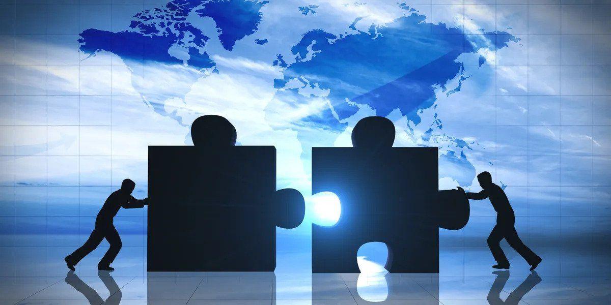 Two silhouetted figures pushing large puzzle pieces together, with a bright light shining through the connection, against a backdrop of a world map on a blue surface.