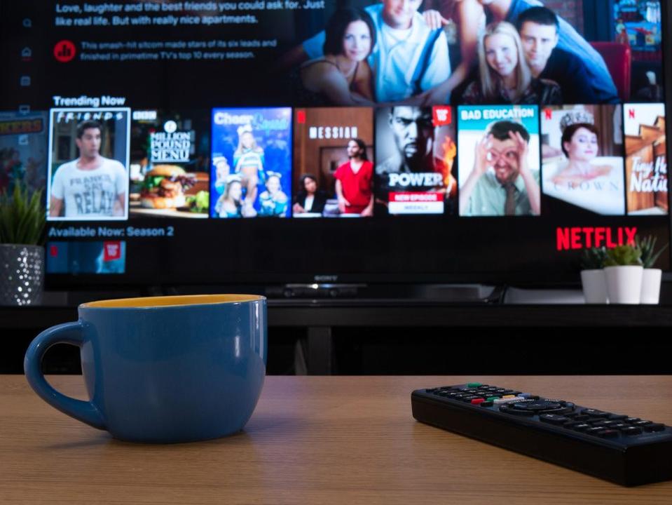  A smart TV displaying Netflix series posters, with a blue coffee cup and remote controller on a table in front of it.