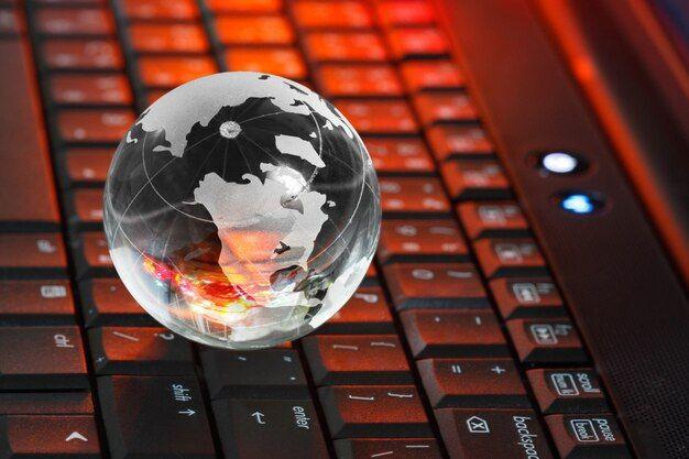 A glass globe sits on top of a computer keyboard, symbolizing the global reach of the internet.
