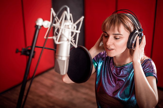 A woman wearing headphones in a recording studio, focused on her work.