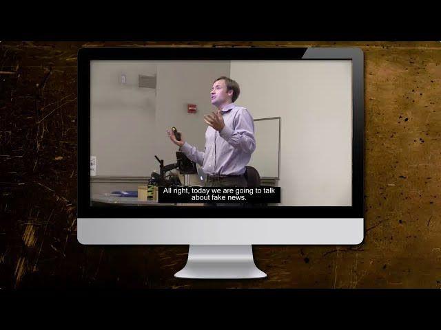 A computer screen shows a man giving a lecture, holding a clicker. The subtitles read: 