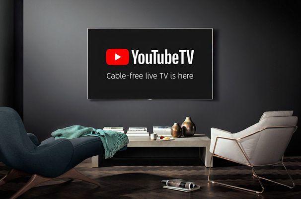 A modern living room with a large flat-screen tv displaying the youtube tv logo, flanked by stylish chairs and minimal decor.
