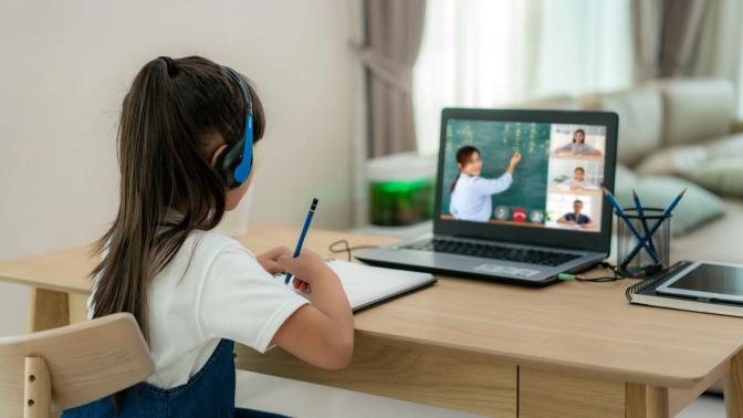 A girl sitting at a desk with headphones on, focused on her laptop screen.