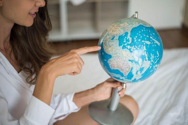 A woman in a white blouse points at a location on a globe she is holding.