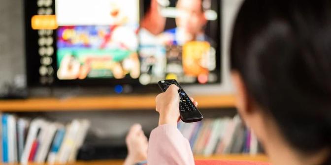 A woman holding a remote control, engrossed in watching television.